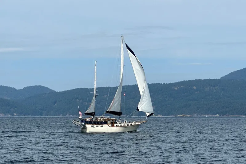Slide: The Image of 1980 Nauticat Pilothouse sailboat cruising on a serene lake with forested hills. - 57