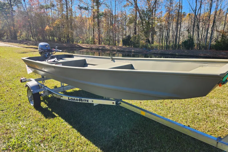 Slide: The Image of 2026 Tracker Grizzly 1436 Utility boat on Load Rite trailer by a pond. - 3