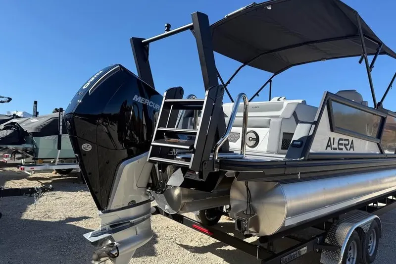 Slide: The Image of 2026 Alera M 23L pontoon boat with Mercury outboard motor, parked on a trailer. - 5