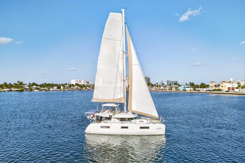The Image of 2021 Lagoon 46 Owner's Version catamaran sailing on a sunny day near coastal cityscape. - 0