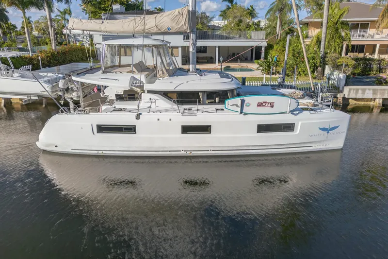 Slide: The Image of 2021 Lagoon 46 Owner's Version catamaran docked in a serene waterfront setting. - 122