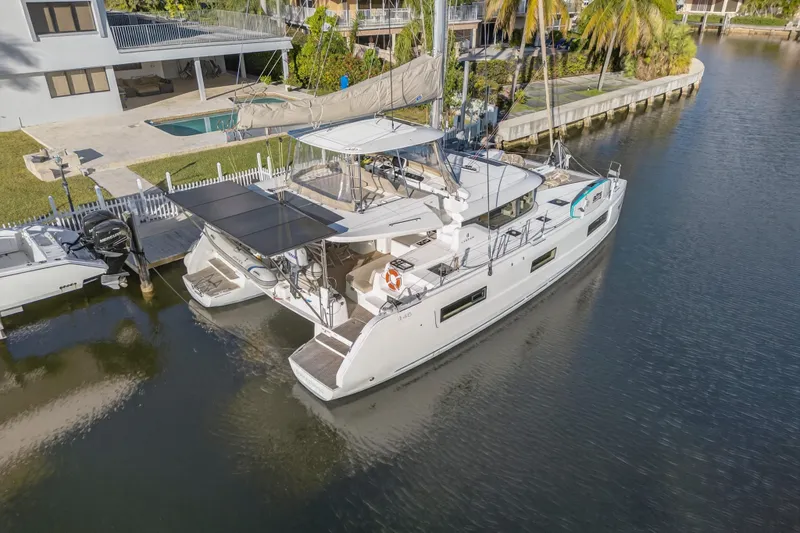 Slide: The Image of 2021 Lagoon 46 Owner's Version catamaran docked in a serene waterfront setting. - 123