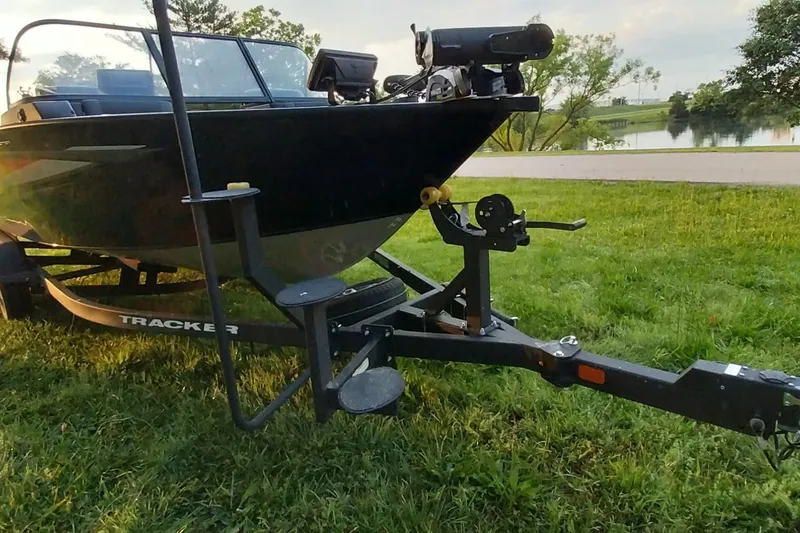 Slide: The Image of 2025 Tracker Targa V-19 WT boat on trailer, parked on grassy area near water. - 28