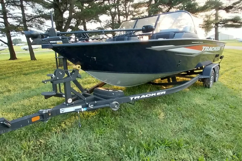 Slide: The Image of 2025 Tracker Targa V-19 WT boat on trailer, parked on grass with trees in background. - 30