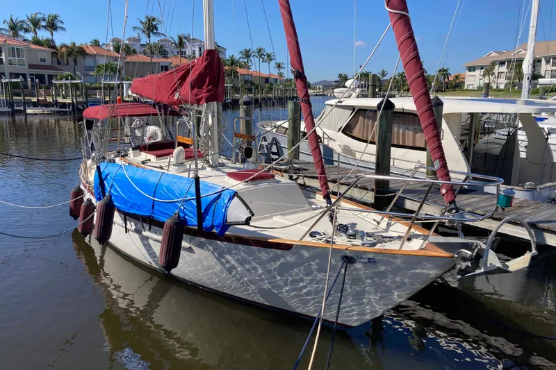 Slide: The Image of 1990 Pacific Seacraft 34 Voyager sailboat docked in a marina, featuring red sails and blue cover. - 3