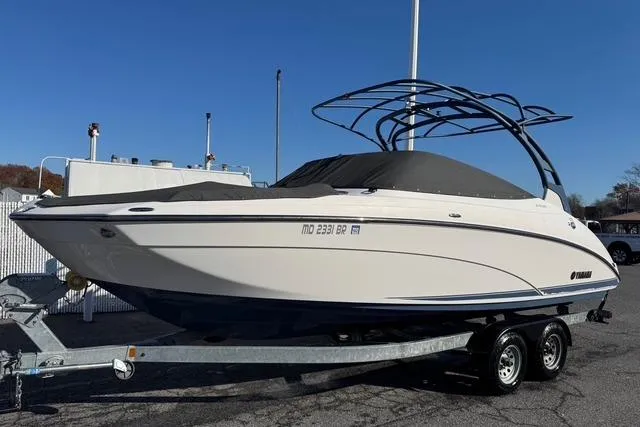 The Image of 2020 Yamaha Boats 242SE on trailer, covered, with sleek design and dual-axle wheels. - 0