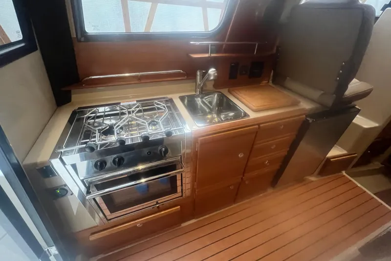Slide: The Image of 2020 Ranger Tugs R-27 Luxury Edition Tug kitchen with stove, sink, and wooden cabinetry. - 2