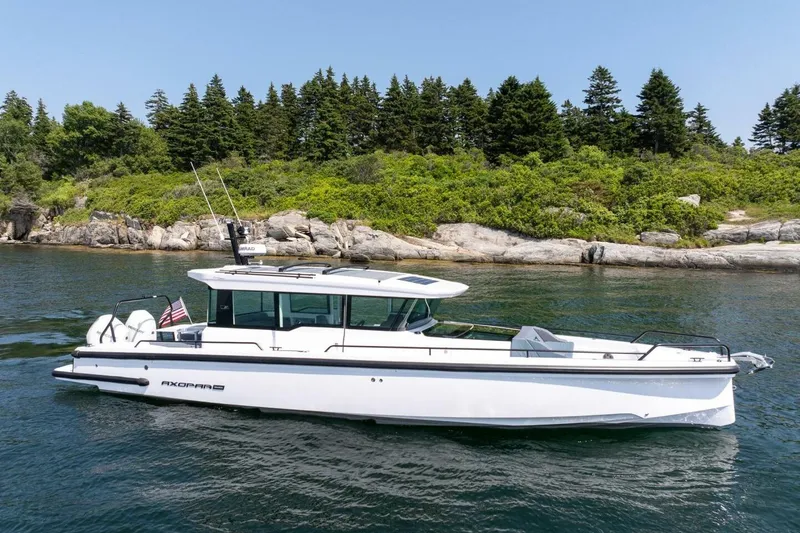 Slide: The Image of 2026 Axopar 37 U-Sofa boat on calm water near wooded shoreline. - 11