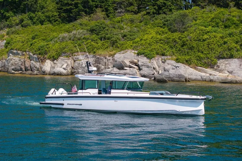 Slide: The Image of 2026 Axopar 37 U-Sofa boat on calm water near green coastline. - 14