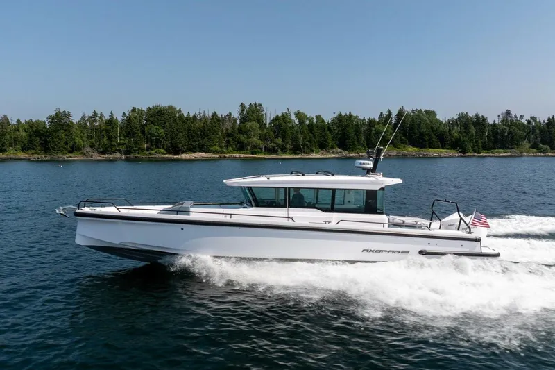 Slide: The Image of 2026 Axopar 37 U-Sofa boat cruising on water with forested background. - 5