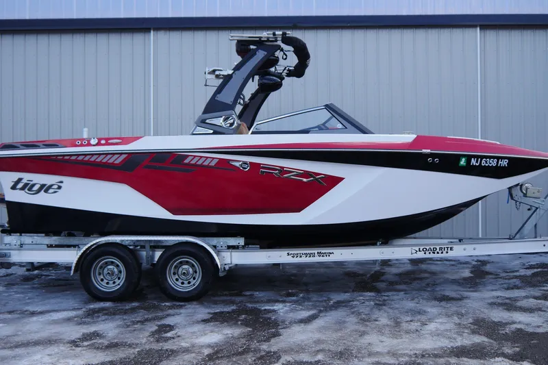 Slide: The Image of 2017 Tigé RZX2 boat in red and white on a trailer, parked outside a building. - 5