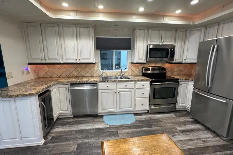 Slide: The Image of Modern kitchen with stainless steel appliances, granite countertops, and white cabinets in a Sharpe 16x90 model. - 4