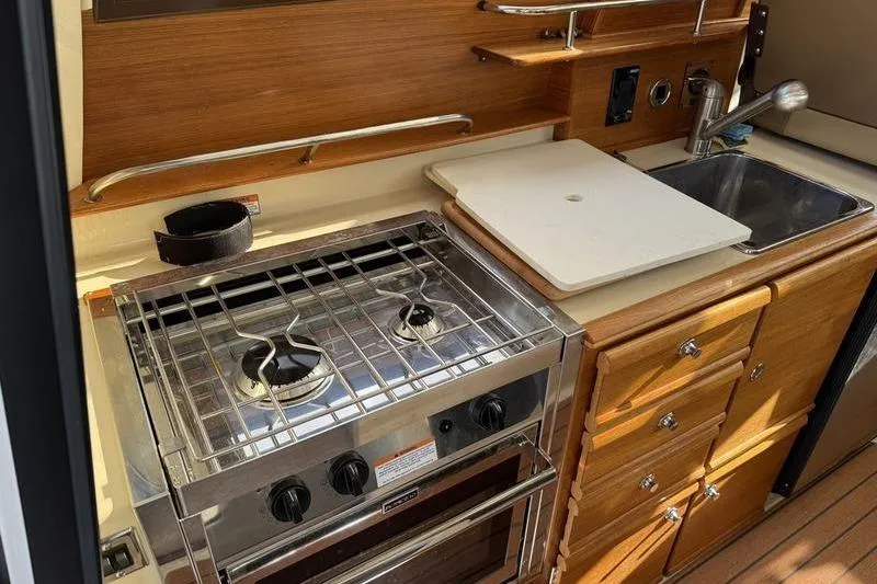 Slide: The Image of 2021 Ranger Tugs R-27 boat kitchen with stove, sink, and wooden cabinetry. - 12