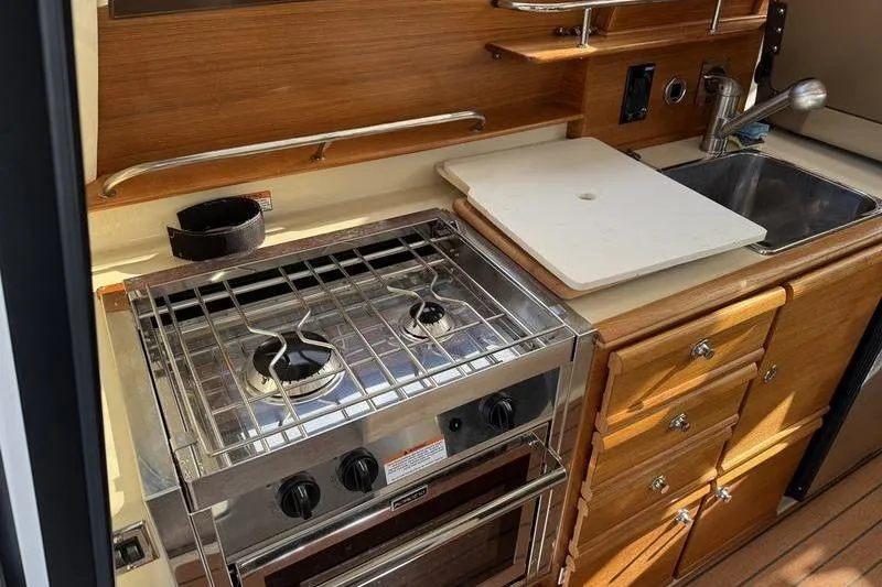 Slide: The Image of 2021 Ranger Tugs R-27 kitchen with stove, sink, and wooden cabinetry. - 14