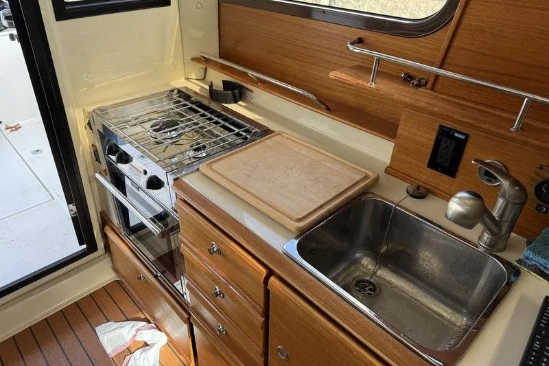 Slide: The Image of 2021 Ranger Tugs R-27 boat kitchen with stove, sink, and wooden cabinetry. - 2