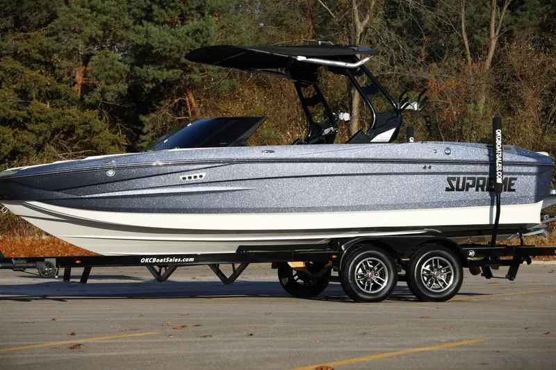 Slide: The Image of 2026 Supreme S220 boat on trailer, parked outdoors with trees in background. - 18