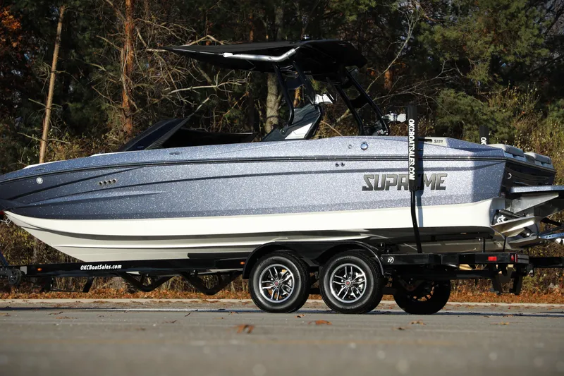 Slide: The Image of 2026 Supreme S220 boat on trailer, parked outdoors with trees in background. - 20