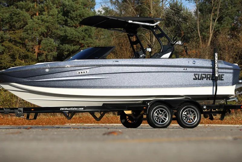 Slide: The Image of 2026 Supreme S220 boat on trailer, parked outdoors with trees in background. - 21