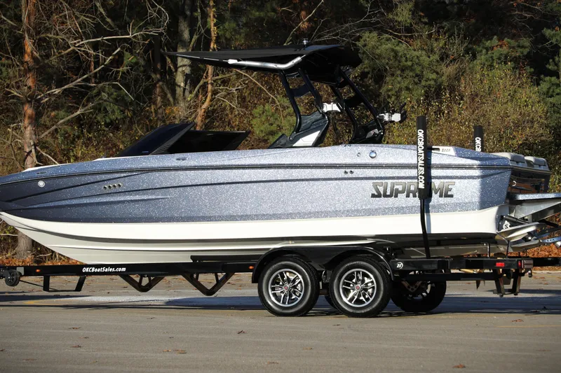 Slide: The Image of 2026 Supreme S220 boat on trailer, parked outdoors with forest background. - 26