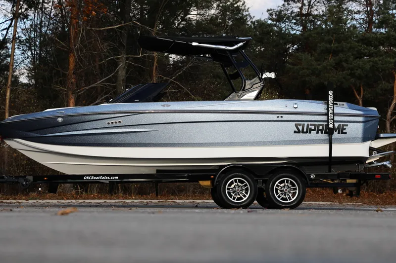Slide: The Image of 2026 Supreme S220 boat on trailer, parked outdoors with forest background. - 29