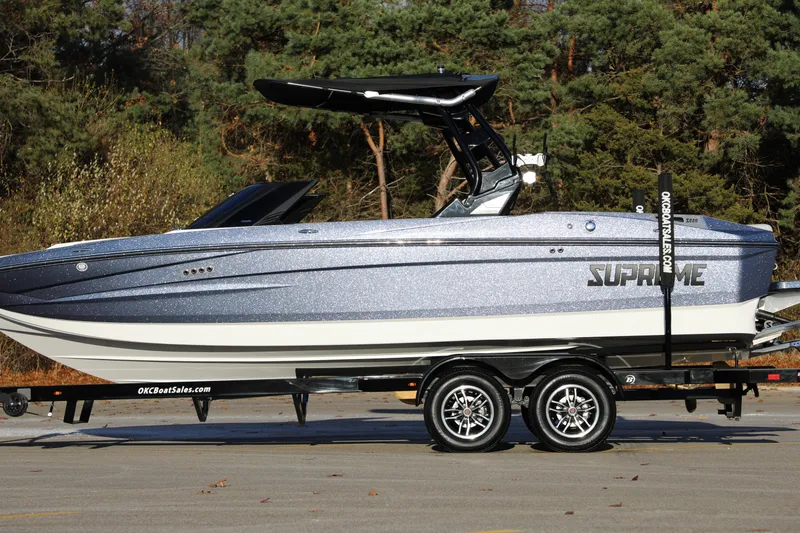 Slide: The Image of 2026 Supreme S220 boat on trailer, parked outdoors with trees in background. - 30