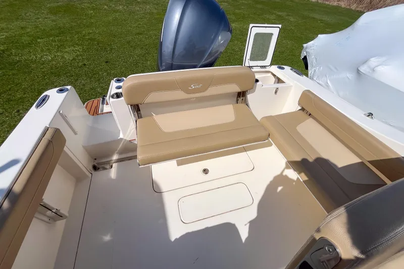 Slide: The Image of 2021 Scout 240 Dorado boat interior with beige seating and motor, parked on grass. - 4