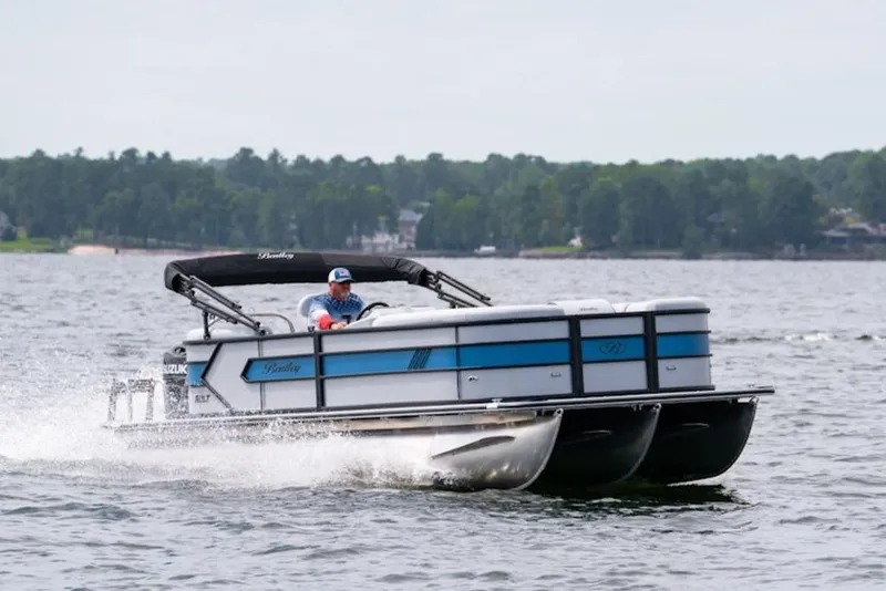Slide: The Image of 2026 Bentley Pontoons 223 Bolt Tri-Toon cruising on a lake with lush green shoreline. - 36