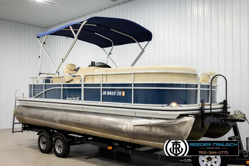 Slide: The Image of 2015 Lowe SS 210 pontoon boat with blue canopy on trailer in indoor showroom. - 3