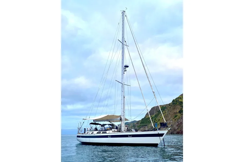 The Image of Sailboat Norseman 447, 1989 model, anchored near a rocky coastline under a cloudy sky. - 1
