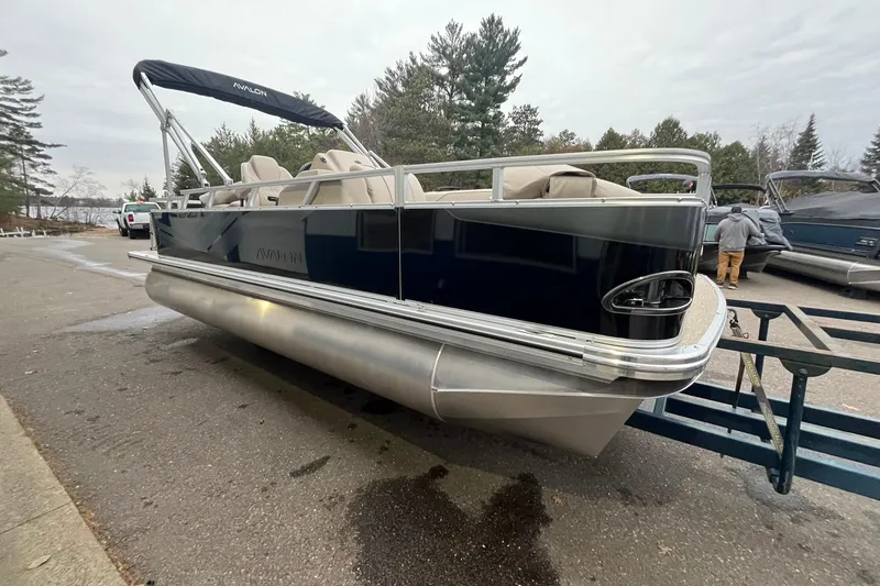 Slide: The Image of 2026 Avalon VTX Quad Fish pontoon boat on trailer, parked near trees. - 5