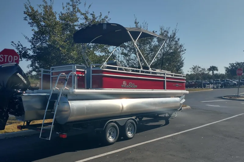 Slide: The Image of 2026 Sun Tracker Fishin' Barge 22 XP3 pontoon boat on trailer in parking lot. - 2