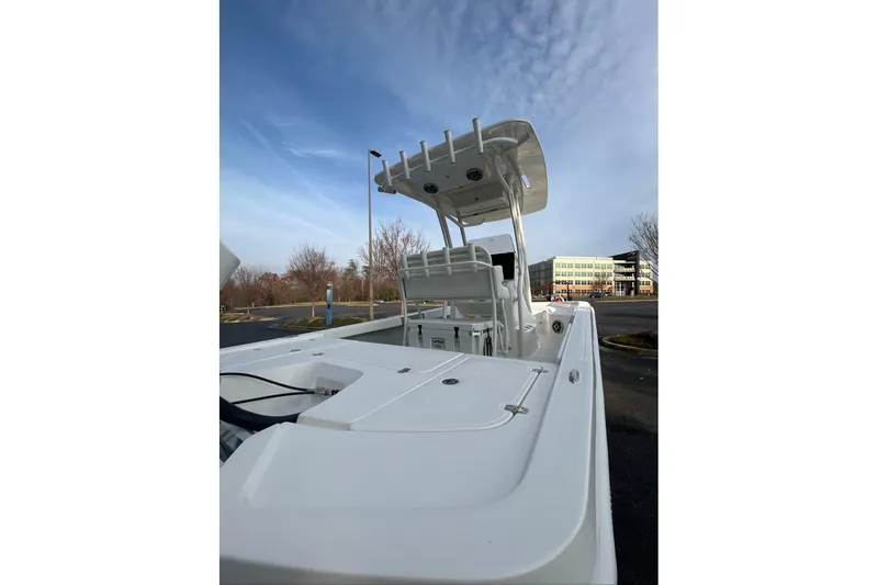 Slide: The Image of 2026 Mako 24 APEX boat with T-top, parked outdoors under a clear sky. - 11