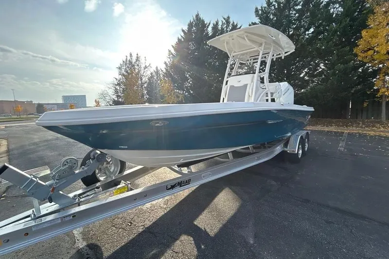Slide: The Image of 2026 Mako 24 APEX boat on trailer, parked outdoors, surrounded by trees. - 7