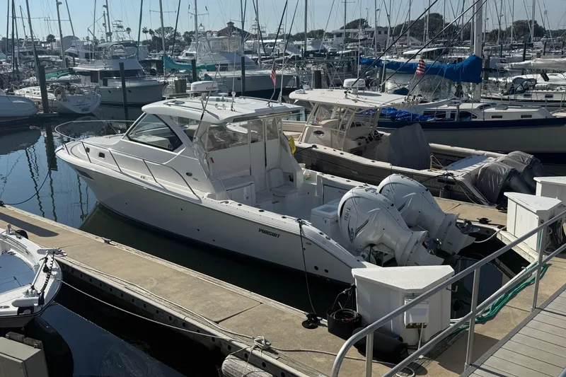 Slide: The Image of 2021 Pursuit OS 355 Offshore boat docked in a marina, surrounded by other vessels. - 56