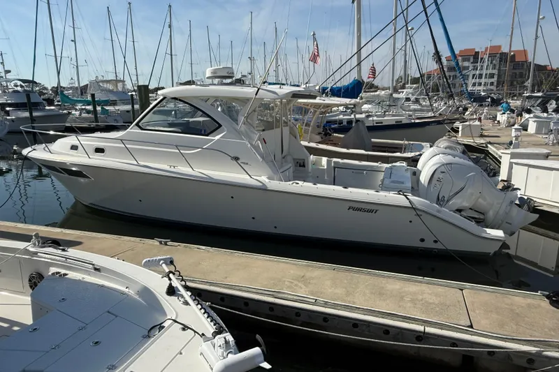 Slide: The Image of 2021 Pursuit OS 355 Offshore boat docked at a marina, surrounded by other vessels. - 57