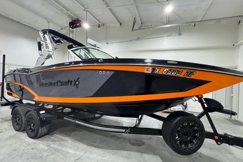 Slide: The Image of 2017 MasterCraft X23 boat with orange and black design on a trailer in a garage. - 11