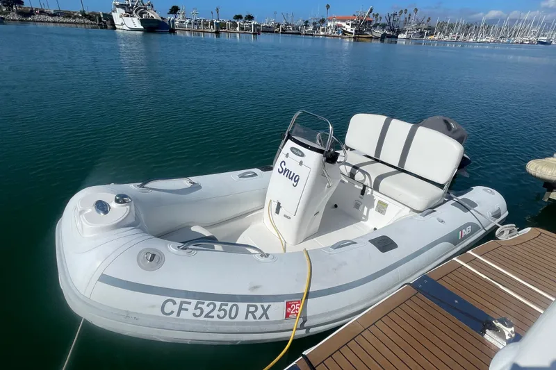 Slide: The Image of A small inflatable boat named "Snug" docked in a marina, with clear blue water. - 76