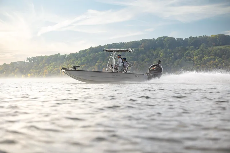 Slide: The Image of 2026 G3 Bay 22 GX boat cruising on a scenic lake with lush green hills. - 2