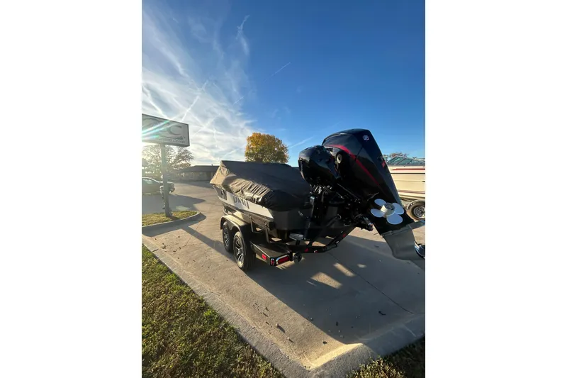 Slide: The Image of 2026 Lund 202 Pro-V GL boat with cover, parked on a sunny day. - 10
