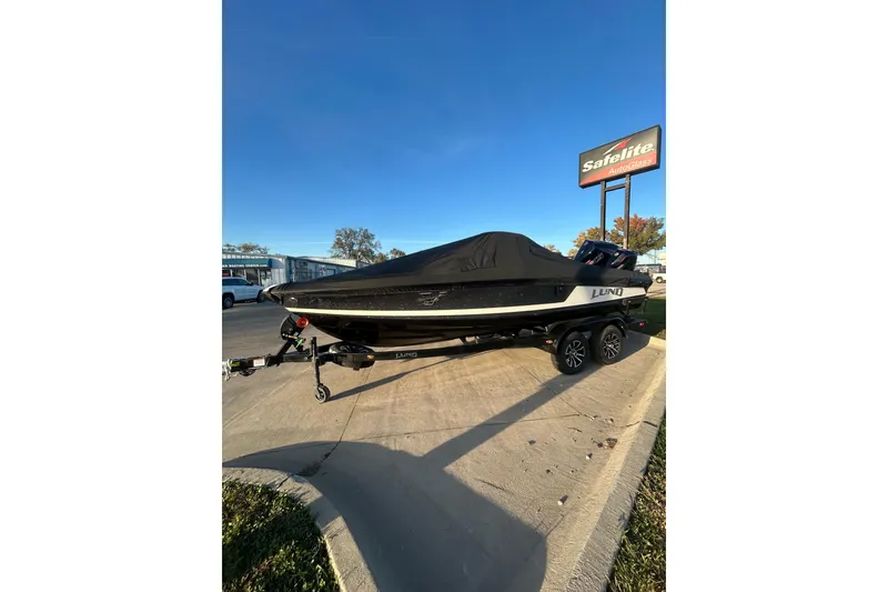 Slide: The Image of 2026 Lund 202 Pro-V GL boat on trailer, covered, parked near Safelite AutoGlass sign. - 9
