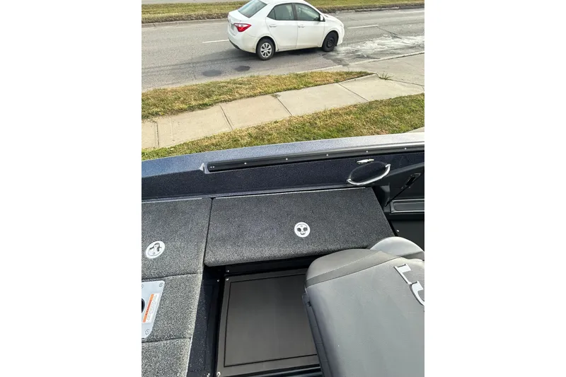 Slide: The Image of 2026 Lund 219 Pro-V GL boat deck with gray carpeting, parked near a sidewalk. - 30