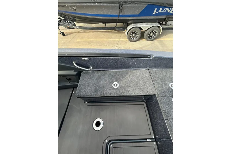 Slide: The Image of 2026 Lund 219 Pro-V GL boat interior storage compartment, open on a sunny day. - 34