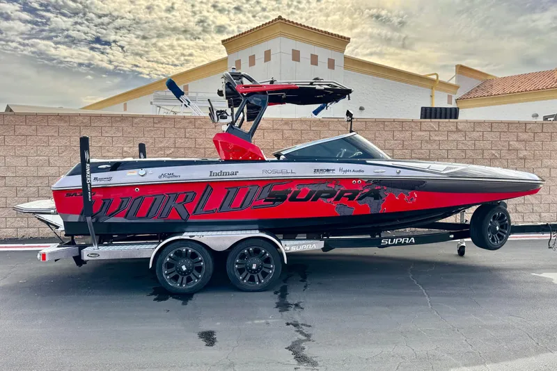 The Image of 2014 Supra SA350 boat on trailer, red and black design, parked outdoors. - 0