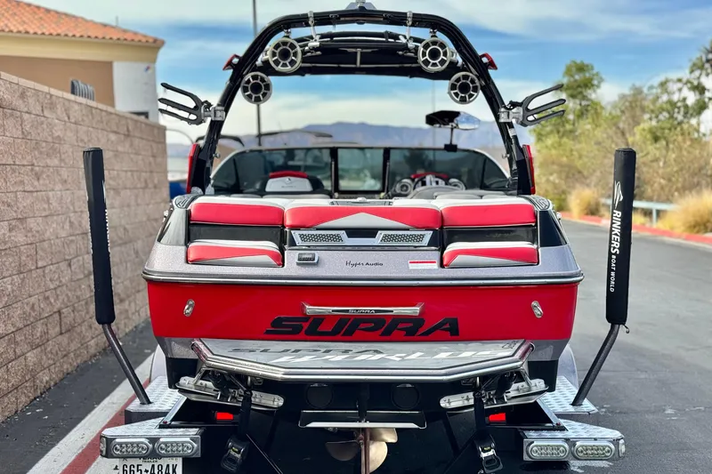 Slide: The Image of Red 2014 Supra SA350 boat with speakers and padded seating, parked on a sunny day. - 4