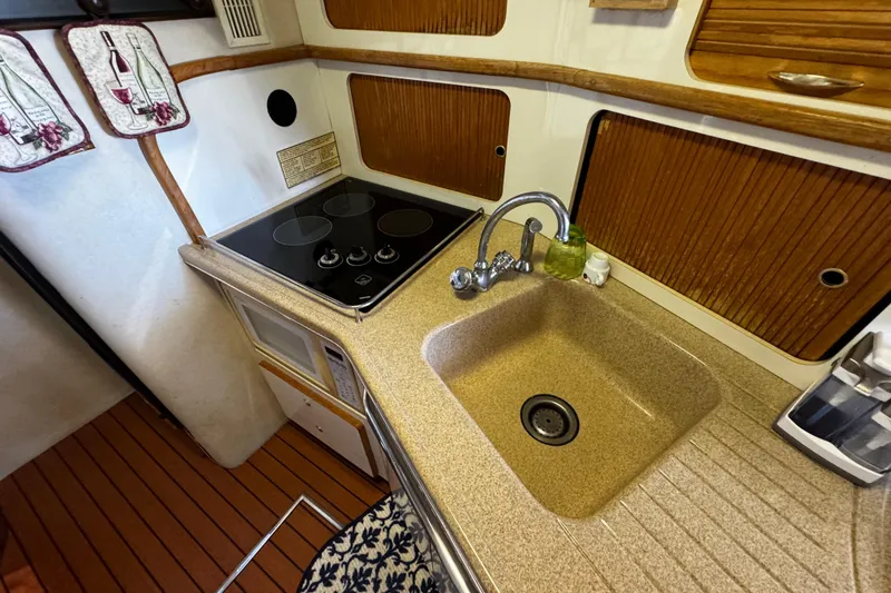Slide: The Image of 1999 Sea Ray 440 Express Bridge kitchen with stove, sink, and wooden cabinetry. - 32