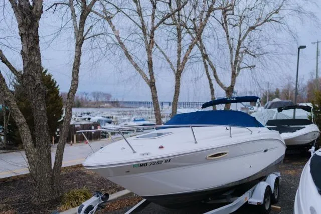 Slide: The Image of 2007 Sea Ray 215 Weekender boat on trailer, parked near marina with trees in background. - 2