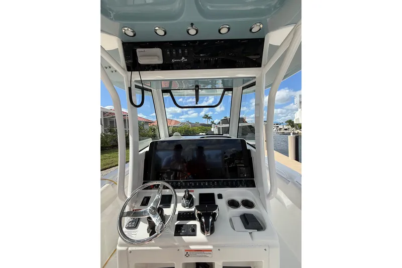Slide: The Image of 2021 Sea Hunt Gamefish 30 boat console with navigation screens, steering wheel, and waterfront view. - 9
