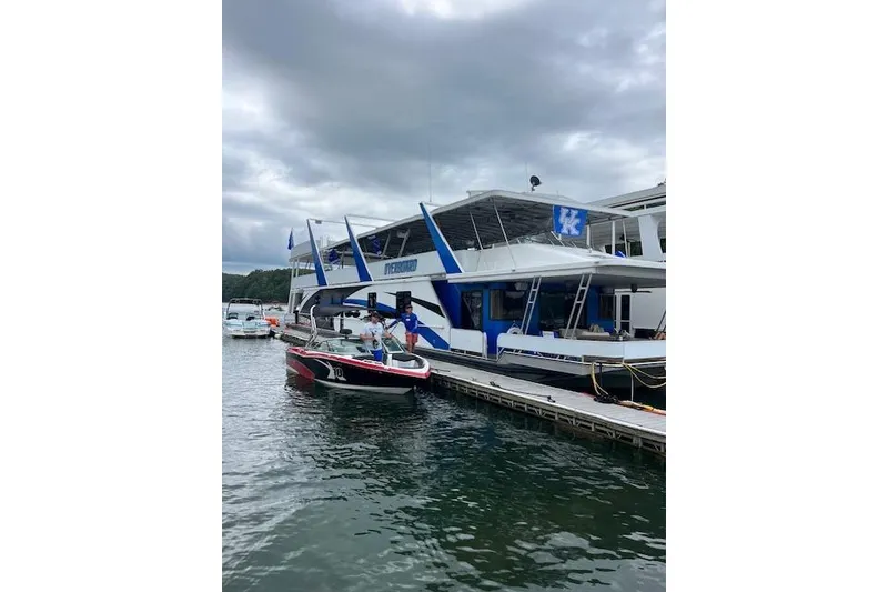 The Image of Houseboat docked on a lake, Sumerset 19.5 x 95, 1995 model, with a small boat nearby. - 0