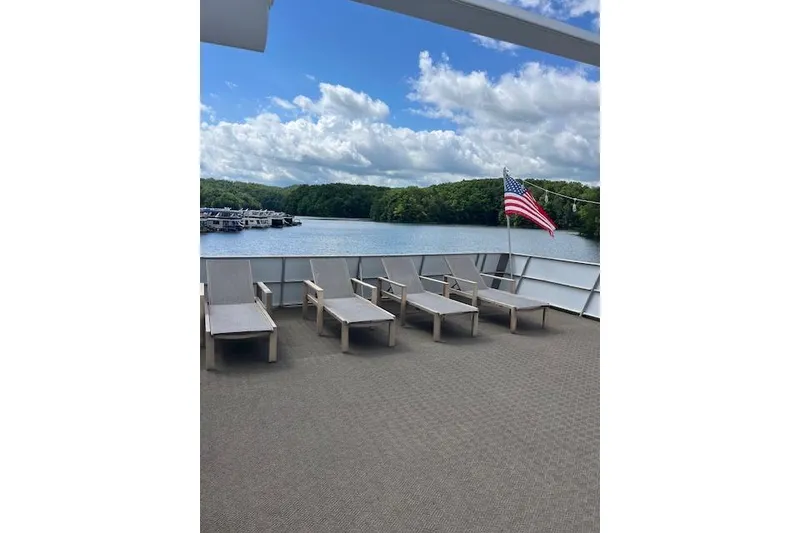 Slide: The Image of Sun deck of 1995 Sumerset houseboat with lounge chairs and American flag, overlooking serene lake. - 32