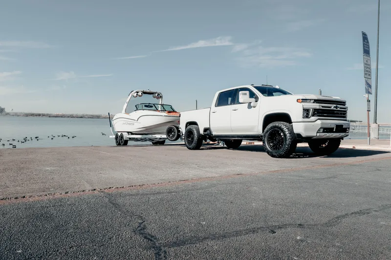 Slide: The Image of White truck towing MB B52 23 Alpha boat, 2026 model, near a lakeside ramp. - 23